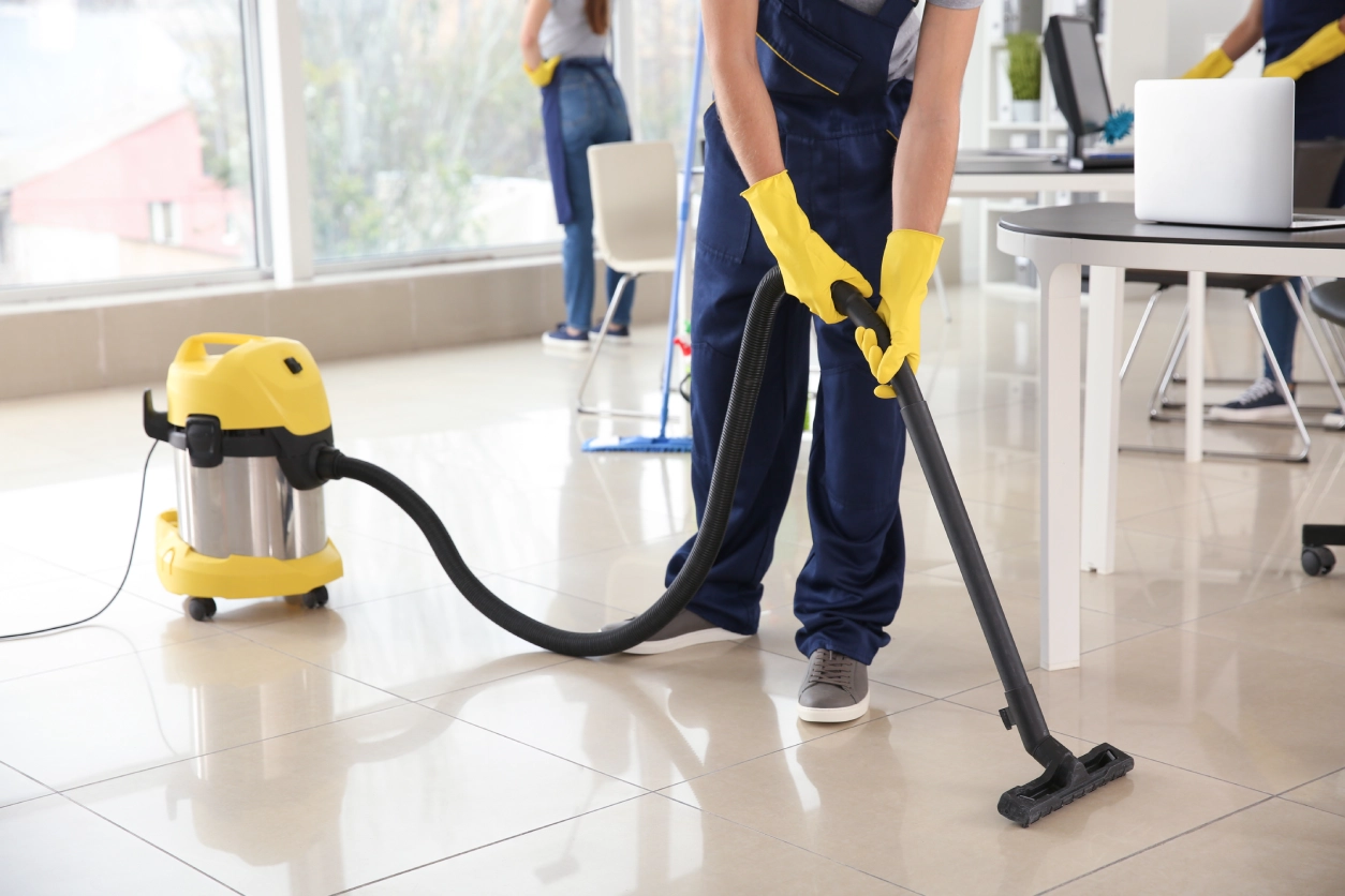 A person in yellow gloves vacuuming the floor.